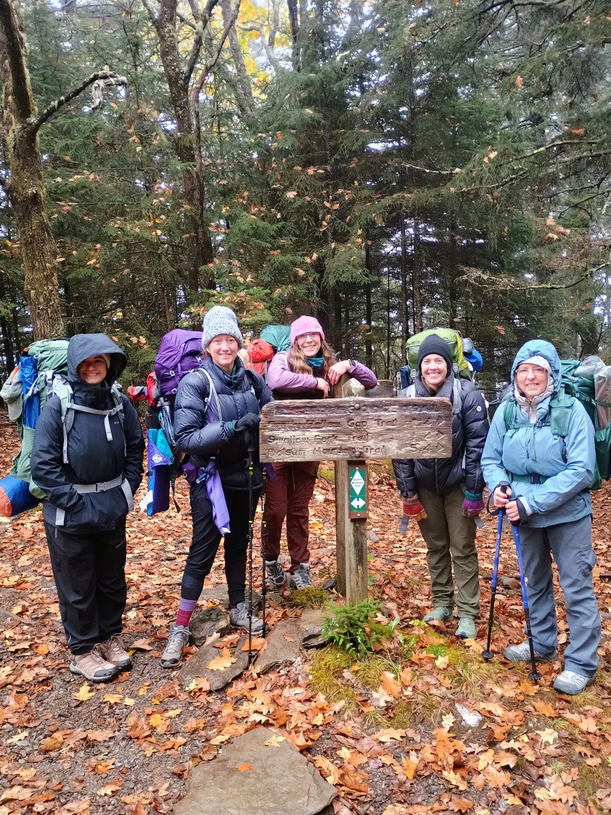 The 2026 class in their backpacks at a trail sign in the woods