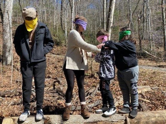 Children blindfolded with bandanas playing a game on a fallen tree